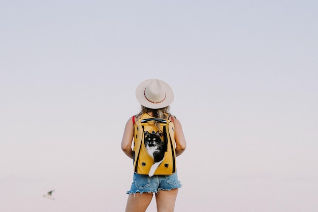 Kostenloses Foto junge frau mit einer katze in einem rucksack am meer. reisekonzept mit einem haustier. katze im rucksack mit bullauge.