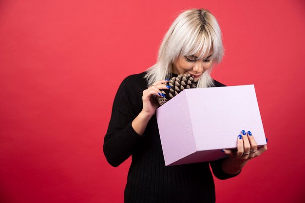 Junge Frau mit Geschenk, das einen großen Tannenzapfen auf einem roten Hintergrund hält. Hochwertiges Foto