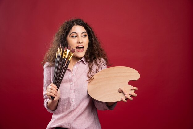 Junge Frau mit glücklichem Ausdruck, der Pinsel und Farbpalette hält.