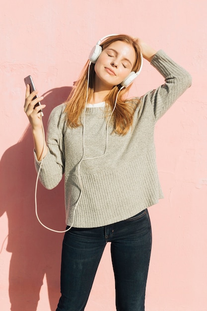 Junge Frau mit ihrem Kopfhörer auf ihrer hörenden Hauptmusik durch Handy