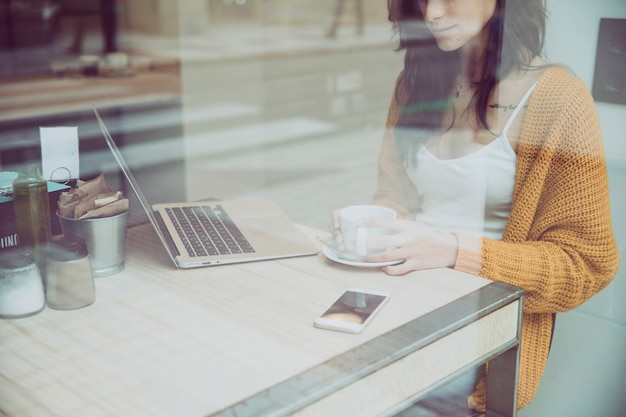 Kostenloses Foto junge frau mit kaffee unter verwendung des laptops im café