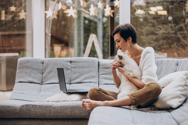 Junge Frau mit Katze, die am Laptop von zu Hause aus arbeitet