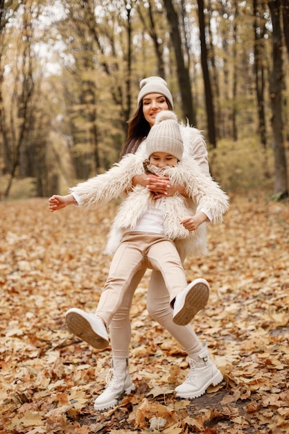 Junge Frau mit kleinem Mädchen, das im Herbstwald steht. Brünette Frau spielt mit ihrer Tochter. Mädchen mit beigem Pullover und Mutter mit weißer Kleidung.