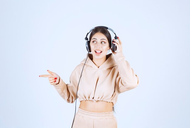 Junge Frau mit Kopfhörern, die jemanden auf der linken Seite zeigen oder bemerken