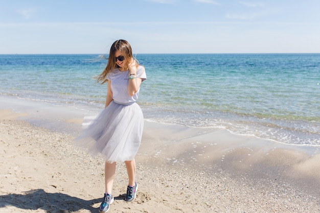 Junge Frau mit langen Haaren geht nahe blauem Meer