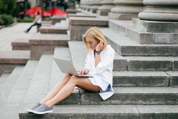 Junge Frau mit Laptop-Computer und Smartphone. Schöne Studentin arbeitet am Laptop im Freien
