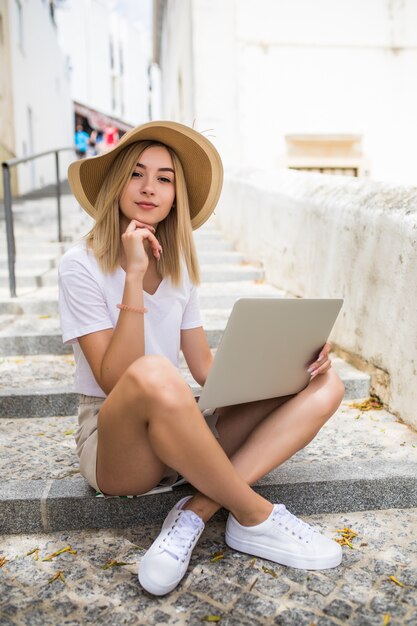 Junge Frau mit Laptop sitzt auf Treppen im Freien