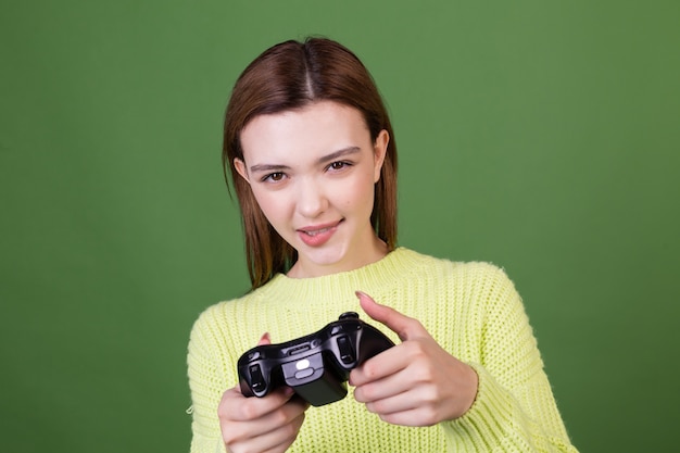 Kostenloses Foto junge frau mit perfektem natürlichem make-up braune große lippen in lässigem pullover an grüner wand mit joystick, der videospiele spielt