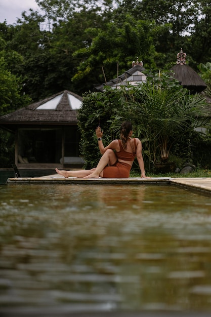 Junge frau mit positiver körperausstrahlung, die yoga allein an deck am pool auf der tropischen insel bali, indonesien, praktiziert. sport, fitness, gesundes lifestyle-konzept.