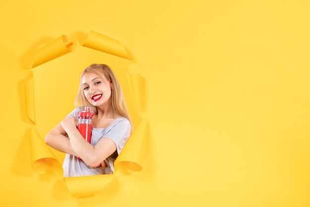 Junge Frau mit roter Flasche an gelber Wand