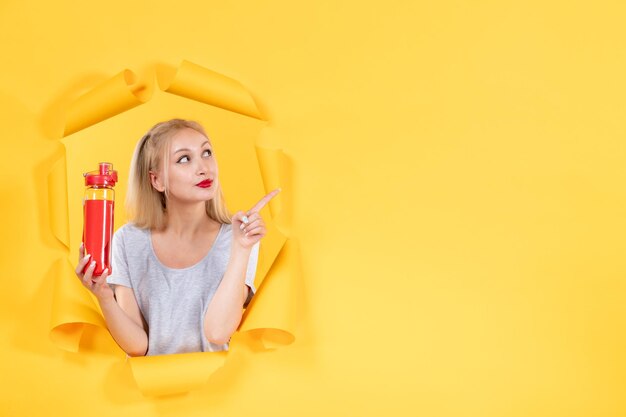 Junge Frau mit roter Flasche an gelber Wand