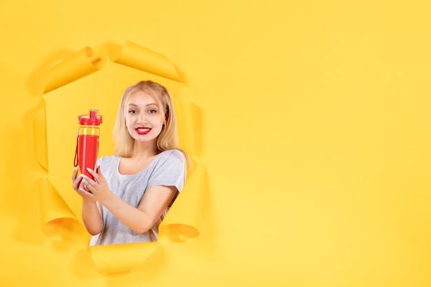Junge frau mit roter flasche auf gelbem hintergrund gesichtsfit-sport-fitnessstudio