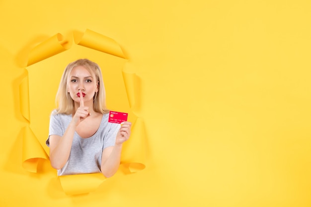 Junge frau mit roter kreditkarte auf zerrissener gelber papieroberfläche