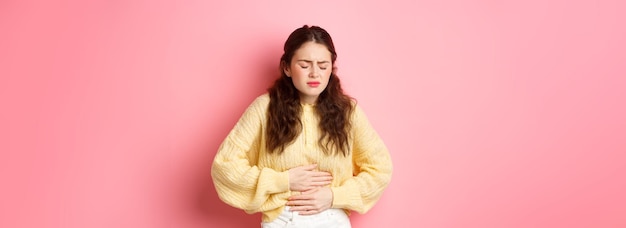 Kostenloses Foto junge frau mit schmerzen im magen, die hände auf dem bauch hält und schreckliche menstruationsbeschwerden spürt, steht