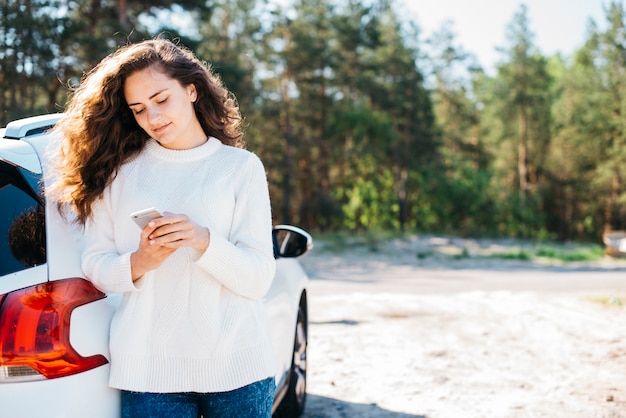 Junge Frau mit Smartphone neben ihrem Auto