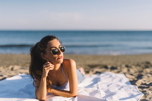 Junge Frau mit Sonnenbrille am Strand liegen