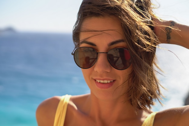Junge Frau mit Sonnenbrille gut gelaunt im Urlaub am Strand einen heißen Sommertag genießen