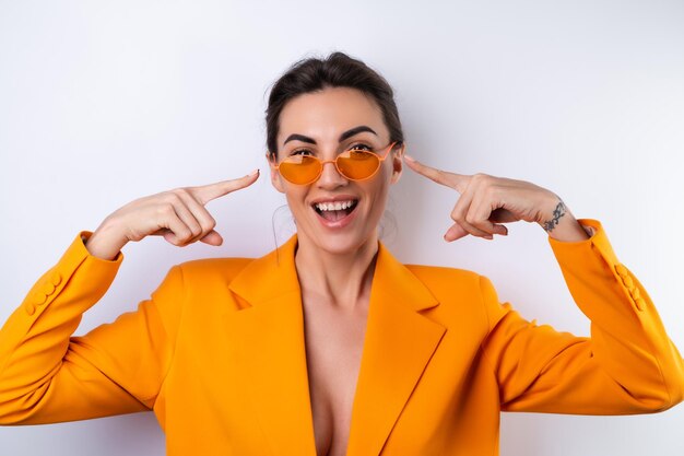 Junge Frau mit trendiger, stylischer Brille und einer leuchtend orangefarbenen, übergroßen Jacke auf weißem Hintergrund