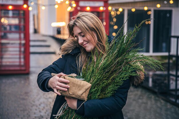 Junge Frau mit Weihnachtsbaum und Geschenkbox auf verschwommenem Hintergrund