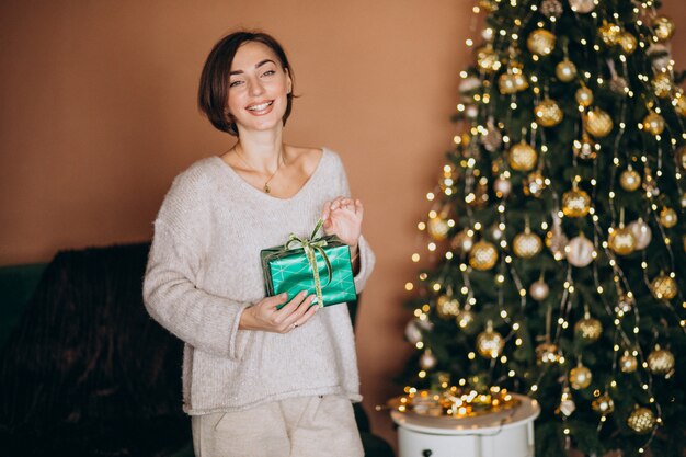 Junge Frau mit Weihnachtsgeschenk durch den Weihnachtsbaum