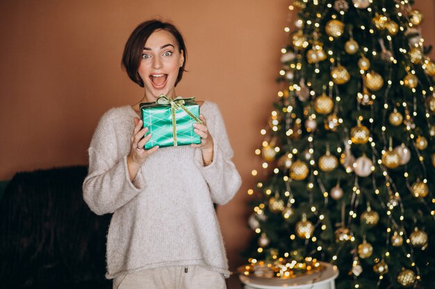 Junge Frau mit Weihnachtsgeschenk durch den Weihnachtsbaum