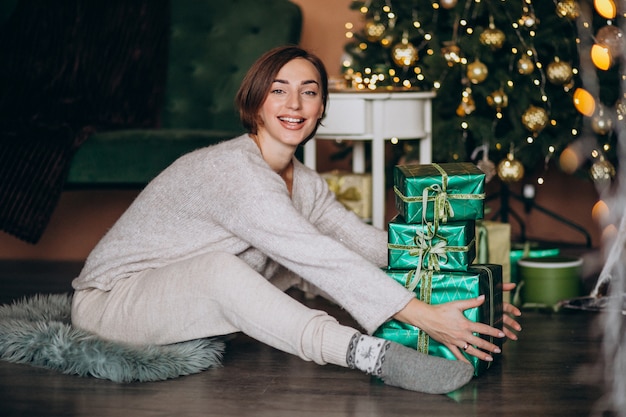 Junge Frau mit Weihnachtsgeschenk durch den Weihnachtsbaum