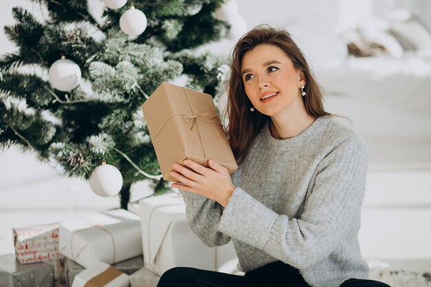 Junge Frau mit Weihnachtsgeschenken durch den Weihnachtsbaum