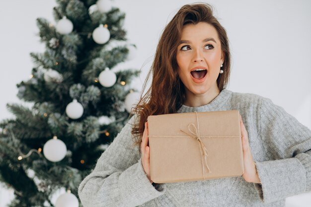 Junge Frau mit Weihnachtsgeschenken durch den Weihnachtsbaum