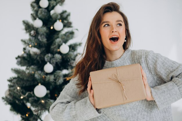 Junge Frau mit Weihnachtsgeschenken durch den Weihnachtsbaum