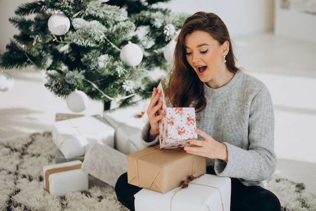 Junge Frau mit Weihnachtsgeschenken durch den Weihnachtsbaum