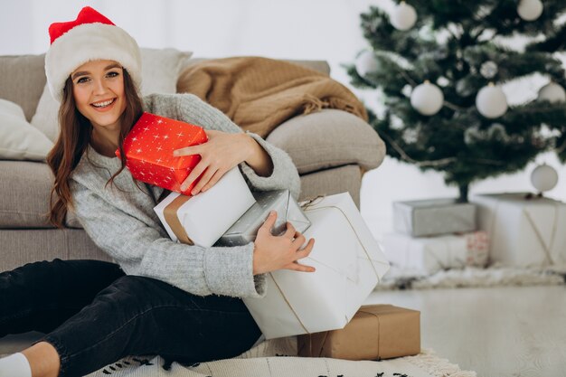 Junge Frau mit Weihnachtsgeschenken durch den Weihnachtsbaum