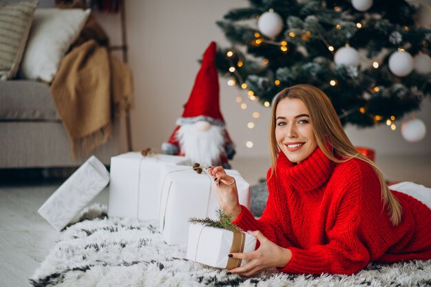 Junge Frau mit Weihnachtsgeschenken durch den Weihnachtsbaum