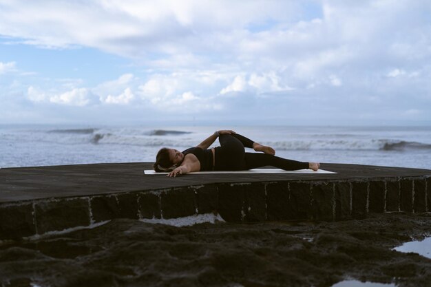 Junge Frau praktiziert Yoga an einem wunderschönen Strand bei Sonnenaufgang. Blauer Himmel, Meer, Wellen, Nähe zur Natur, Einheit mit der Natur.