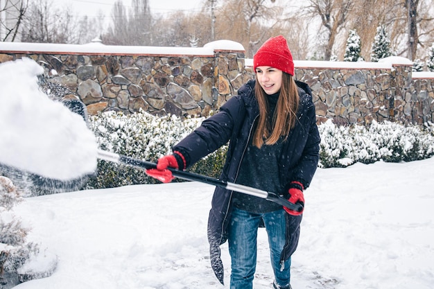 Junge Frau reinigt Schnee im Hof bei Schneewetter