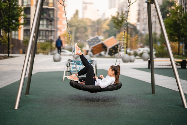 Junge Frau reitet auf einer Schaukel. Mädchen, das auf dem Spielplatz ruht.