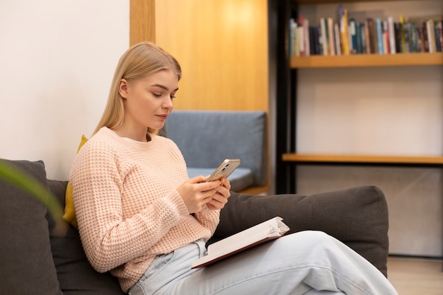 Junge Frau schaut in einer Bibliothek auf ihr Smartphone