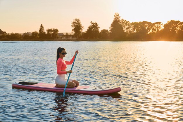 Junge Frau schwimmt bei Sonnenuntergang auf einem Sup-Board