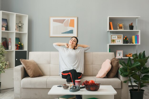 Junge Frau sitzt auf dem Sofa hinter dem Couchtisch im Wohnzimmer