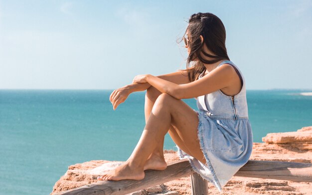 Junge Frau sitzt auf einer Planke und beobachtet das Meer tagsüber