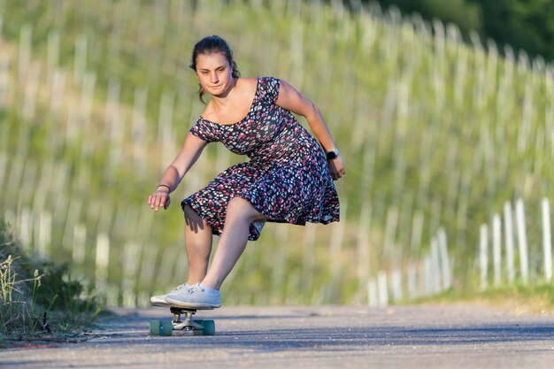 Junge Frau skateboarding auf einer leeren Straße, die durch Grün umgeben ist