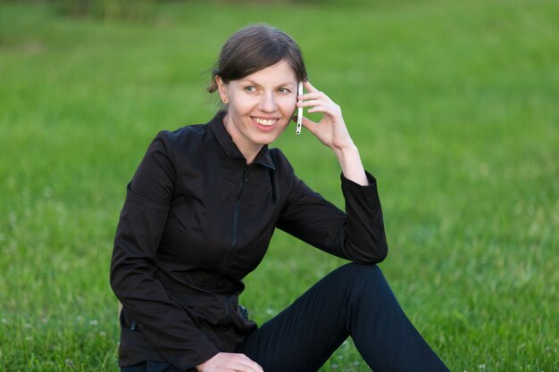 Junge Frau spricht auf Handy sitzt auf Gras