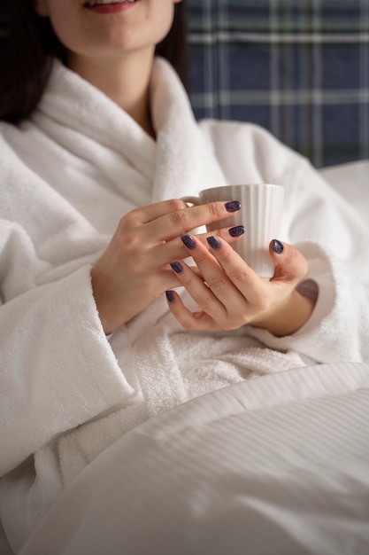 Junge Frau trinkt Kaffee, während sie auf dem Bett in einem Hotelzimmer sitzt