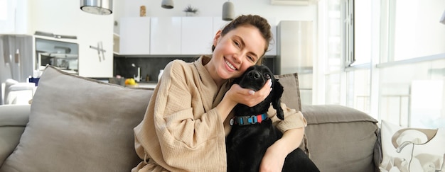 Kostenloses Foto junge frau umarmt entzückenden hund und kuschelt ihren welpen zu hause auf dem sofa