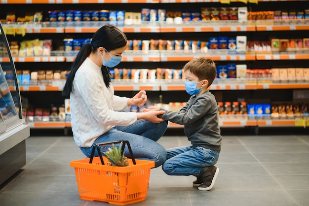 Junge frau und ihr kind, die schützende gesichtsmasken tragen, kaufen ein lebensmittel in einem supermarkt ein