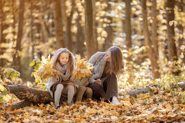 Junge Frau und kleines Mädchen und Junge, die im Herbstwald spazieren. Frau, ihre Tochter und ihr Sohn spielen und Spaß haben. Mädchen, das braunes Kleid trägt.