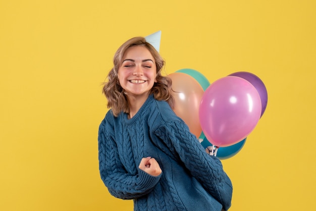 junge Frau versteckt bunte Luftballons hinter ihrem Rücken auf gelb