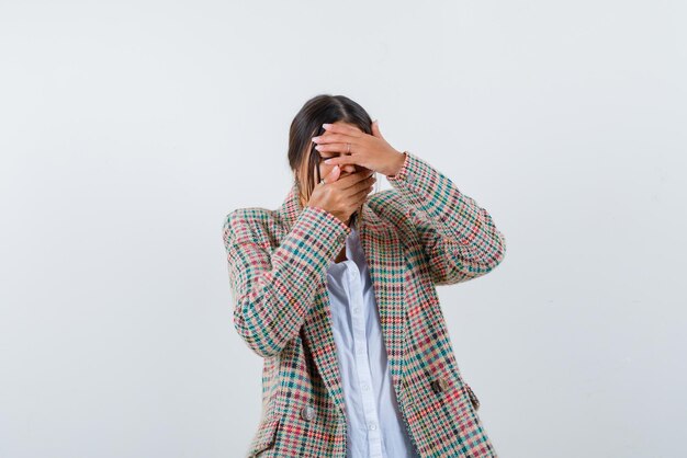 Junge Frau versteckt ihr Gesicht mit den Händen auf weißem Hintergrund