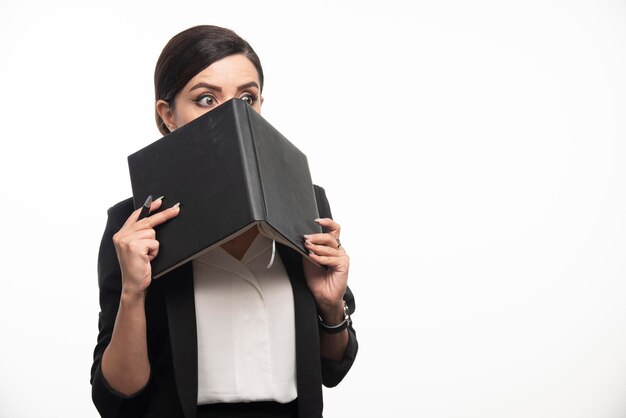 Junge Frau versteckt sich hinter Buch auf weißem Hintergrund. Foto in hoher Qualität