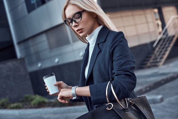 Junge frau wäscht an ihrer armbanduhr in einer ihrer handkaffee in einer anderen handtasche