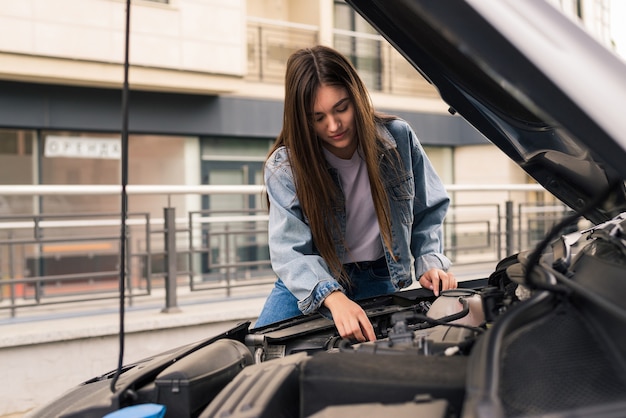 Kostenloses Foto junge frau wartet auf hilfe in der nähe ihres autos, das am straßenrand kaputt ist.